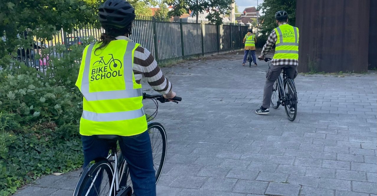 Volwassen van de Brainport Bike School oefenen met fietsen onder begeleiding van een instructeur.